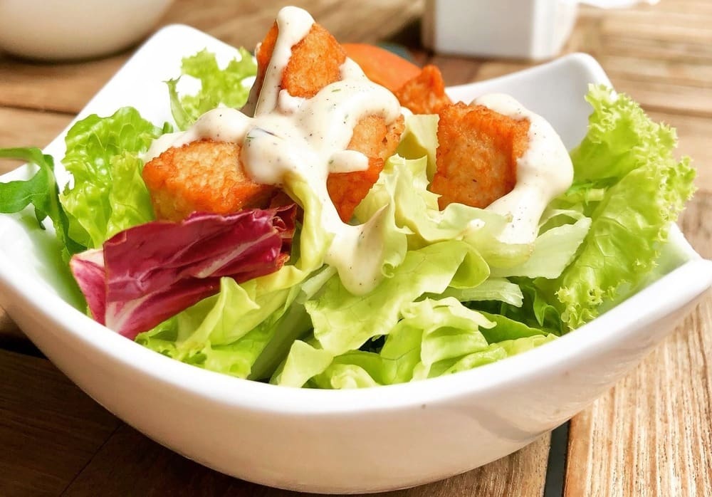 A salad in a bowl with dressing on the side.
